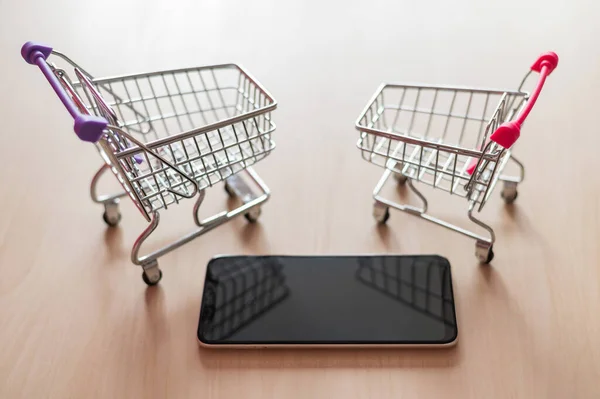 Vista superior en un carrito de la compra y teléfono móvil en una mesa de madera. Compras en línea Smartphone. Compras online . —  Fotos de Stock