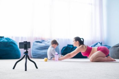 Hamile bir kadın oğluyla jimnastik yapıyor. Müstakbel anne telefonda blogu için bir eğitim videosu çekiyor. Bebekli fitness.