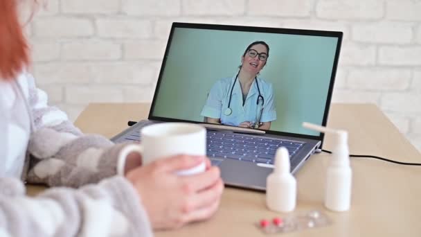 女が病気休暇中です。患者はオンラインで医者に相談する。ラップトップ上の医師とビデオチャット。セラピストは病気を治療するためのヒントを与えます. — ストック動画