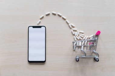 Telefonunda haplar ve uyuşturucular olan bir alışveriş arabası. Uzaktan uyuşturucu alımı. Çevrimiçi eczane kavramı. Siyah ekranlı akıllı telefon.