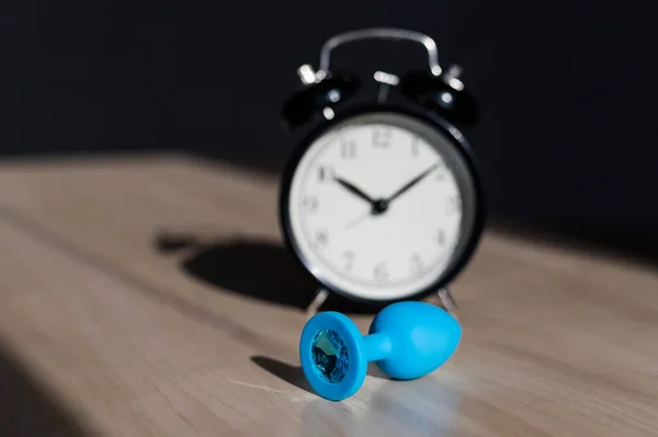 Modrý latexový anální kolík s krystaly a budíkem na dřevěném stole. Čas tělesných rozkoší. — Stock fotografie