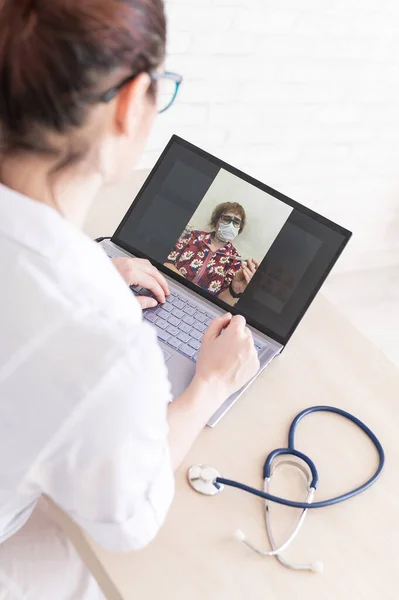 An elderly woman with the flu for an online consultation with a doctor. Female practitioner makes a video call with a patient on a laptop. A pensioner on the remote doctors office.