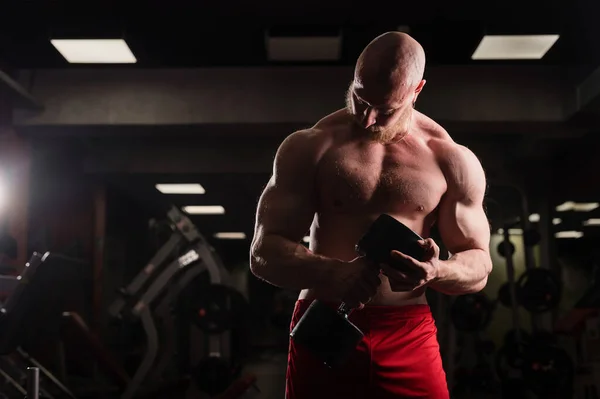 Póló nélküli jóképű férfi bicepsszel és mellkas gyakorlattal súlyzóval. Macho srác testépítő. Izomtréner az edzőteremben. — Stock Fotó