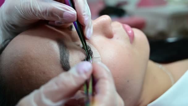 Asian woman lies on a couch during eyelash extension procedure. Master and model on a beauty procedure. — Stock Video