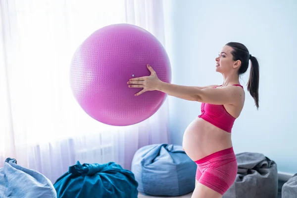 Těhotná žena ve sportovním oblečení dělá gymnastiku pro těhotné ženy. Dívka je zapojena do fitness s míčem pro nastávající matky. Poslední trimestr. — Stock fotografie