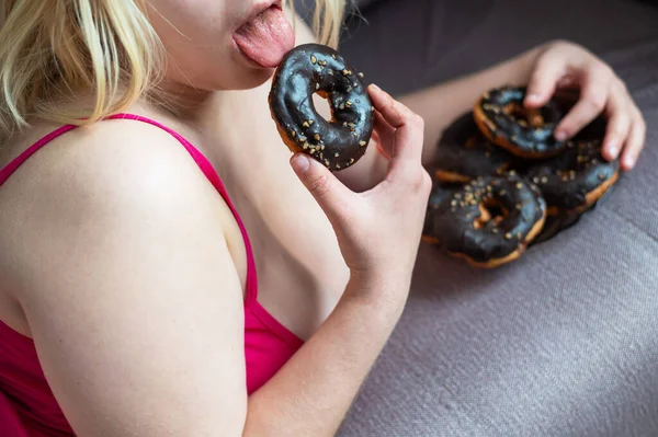 Bionda grassa mangia una ciambella al cioccolato. Giovane donna obesa irriconoscibile che si gode dolci panini a colazione. Foto ritagliata . — Foto Stock