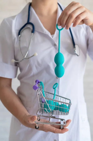 Um ginecologista sem rosto coloca um conjunto de bolas vaginais em um carrinho de compras em miniatura. O médico detém um mini carrinho e dispositivo para os músculos do assoalho pélvico. Conceito de saúde feminina. Kegel brinquedo — Fotografia de Stock