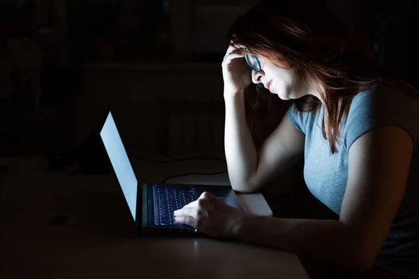 Une femme fait des heures supplémentaires. Un étudiant étudiant sur un ordinateur portable la nuit dans le noir. La fille s'inquiète des problèmes au travail et tient sa main sur son front . — Photo