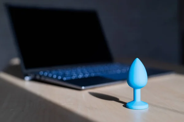 Blue latex anal plug the laptop on the table. The concept of virtual sex on the Internet. Anus extender toy for adults.