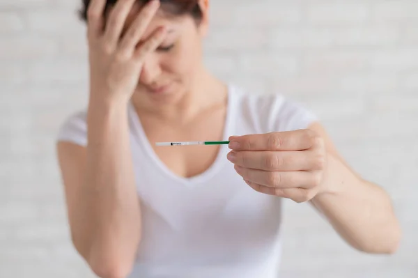 Розчарована жінка показує негативний тест на вагітність. Поняття жіночого безпліддя. Людський хоріонічний гонадотропін. Одна смужка. Невиправдані очікування . — стокове фото