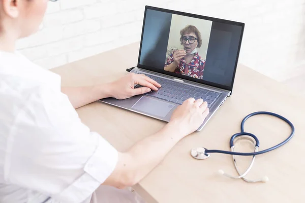 An elderly woman with the flu for an online consultation with a doctor. Female practitioner makes a video call with a patient on a laptop. A pensioner on the remote doctors office.