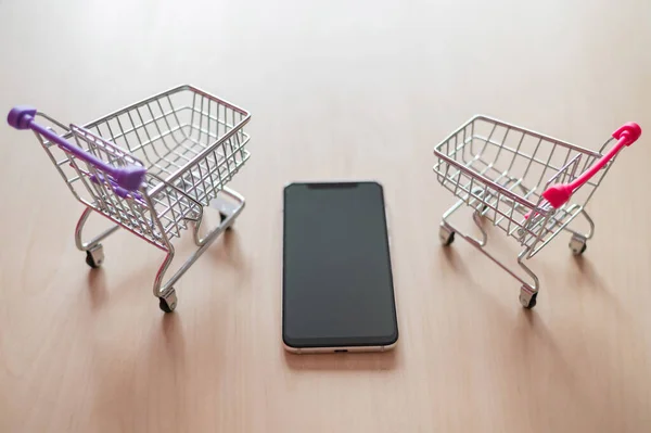 Vista superior em um carrinho de compras e telefone celular em uma mesa de madeira. Smartphone compras online. Compras online . — Fotografia de Stock