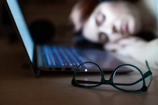 Mujer cansada durmiendo en el lugar de trabajo cerca de la computadora portátil. chica dormida para el trabajo remoto. Un estudiante con exceso de trabajo se quedó dormido sobre la mesa. Gafas en primer plano . —  Fotos de Stock