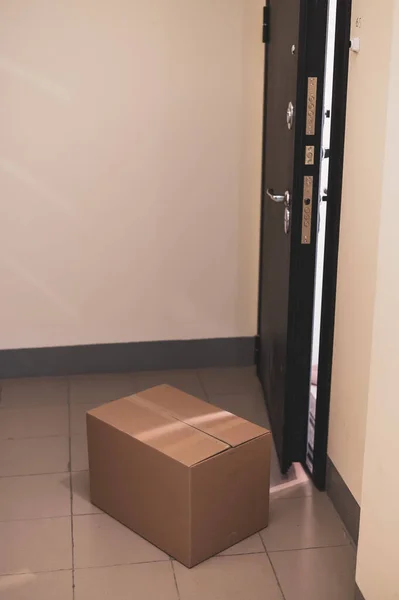 Концепция бесконтактной доставки дверей в карантинный период. Картонная коробка с онлайновой покупкой на открытой входной двери в пустом зале в случае опасности коронавируса . — стоковое фото