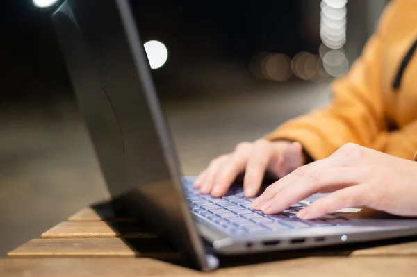 Closeup de mãos femininas em um touchpad de computador. Freelancer trabalha remotamente em um laptop ao ar livre. Uma mulher está estudando na rua à noite . — Fotografia de Stock