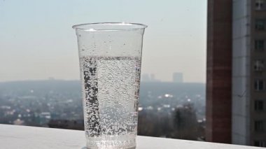 Yavaş çekimde bir dilim limon şeffaf plastik bardağa soda ile düşer. Şehre bakan pencerenin yanında ferahlatıcı bir kokteyl. Sıcak yaz günü.