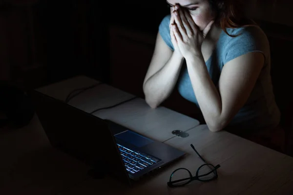 Femme fait des heures supplémentaires. Un étudiant étudiant sur un ordinateur portable la nuit dans le noir. La fille est inquiète des problèmes au travail et tient ses mains sur son visage . — Photo