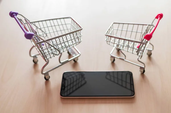 Draufsicht auf einen Einkaufswagen und Handy auf einem Holztisch. Smartphone-Online-Shopping. Online-Einkauf. — Stockfoto