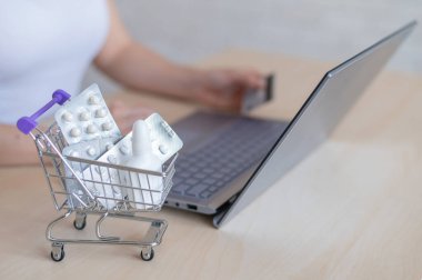 Çevrimiçi eczane kavramı. Bir kadın elinde bir banka kartı tutuyor ve internetten hap alıyor. Kızın biri internetten ev teslimatı yapan bir bilgisayarla ilaç alıyor..
