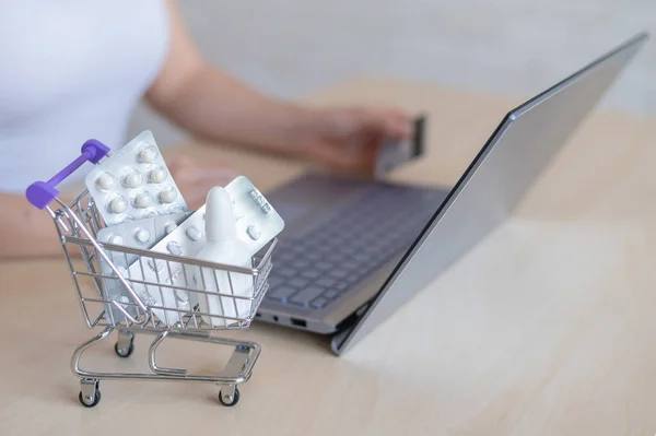 Online pharmacy concept. A woman holds a bank card in her hands and buys pills online. A girl makes an online purchase of pharmaceuticals with home delivery on a laptop.