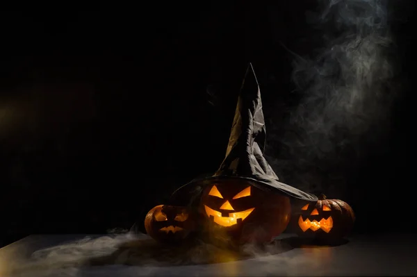 Läskiga orange pumpor för Halloween står i rad på en mörk bakgrund. Jack O Lantern i häxhatt. Mystisk dimma kryper på marken. Bus eller godis. — Stockfoto