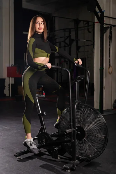 Όμορφη μελαχρινή με ελαστικά οπίσθια ασκήσεις σε ένα ποδήλατο αέρα. Αθλητική γυναίκα που ασχολούνται στο γυμναστήριο σε ένα ποδήλατο άσκηση. — Φωτογραφία Αρχείου