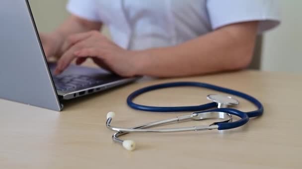 Der gesichtslose Arzt sitzt am Schreibtisch und tippt am Computer. Krankenschwester füllt Bericht auf Laptop aus. Nahaufnahme der Hände auf der Tastatur. — Stockvideo