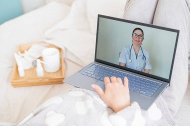 Bir kadın yatağa uzanıyor ve bir terapistin soğuk algınlığı tedavisi hakkında tavsiyelerini dinliyor. Laptopta tıbbi nakli izleyen bir kız. Doktor çevrimiçi danışmanlık yapıyor..