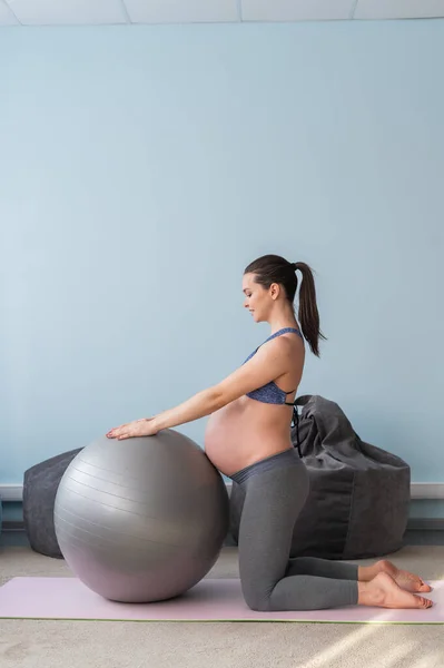 Zwangere Europese vrouw voert oefeningen met fitness bal. Verwachte moeder doet yoga in het derde trimester. Meisje in de klas ter voorbereiding op de bevalling. — Stockfoto