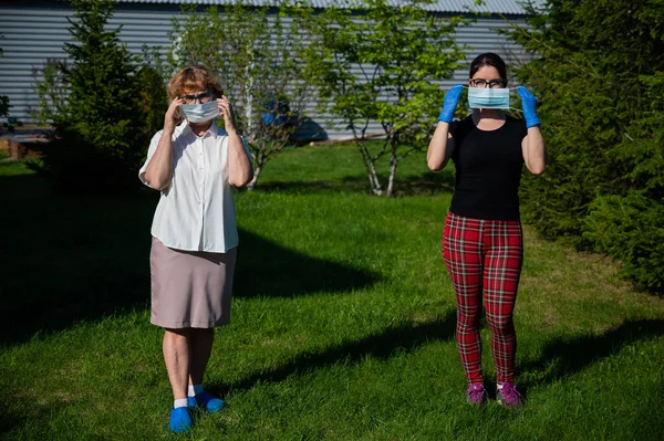 Máma s dcerou si nasadili lékařské masky a pozorovali společenskou vzdálenost. Dvě ženy stojí v parku ve velké vzdálenosti od kamarádky. Proti šíření viru.. — Stock fotografie