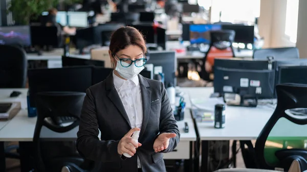 Gestora con mascarilla médica rocía antiséptico en la mano. Una mujer en traje usa un desinfectante para desinfectar. Concepto de trabajo de oficina durante la epidemia de coronavirus . —  Fotos de Stock