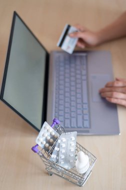Çevrimiçi eczane kavramı. Bir kadın elinde bir banka kartı tutuyor ve internetten hap alıyor. Kızın biri internetten ev teslimatı yapan bir bilgisayarla ilaç alıyor..