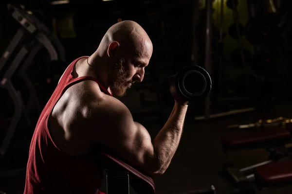 Kopasz, cuki, szakállas férfi bicepszgyakorlatozik. A fiatalember testépítéssel foglalkozik. Edző az edzőteremben izmos karokkal. — Stock Fotó