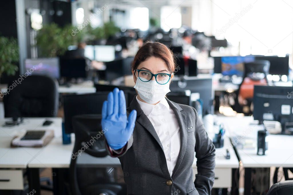 Female office manager in a medical mask and gloves. A woman in a suit uses infection protection. The girl gestures to stop the spread of the coronavirus.