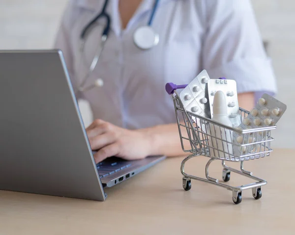 Felismerhetetlen női orvos kinyomtat egy jelentést egy laptopon. Online gyógyszertár koncepció. Az arctalan gyógyszerész drogot árul az interneten. Mini bevásárlókocsi beatery tabletta. — Stock Fotó