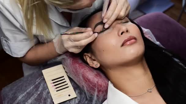 Portrait of a beautiful asian woman with closed eyes during eyelash extension procedure. Double eyelash volume. time lapse. — Stock Video