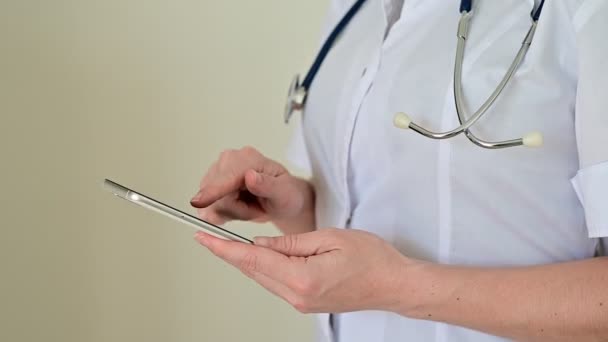 制服を着た認知できない女性医師はタブレットコンピュータを使う。医療従事者がデバイス上の患者と連絡を取ります。作物だ. — ストック動画
