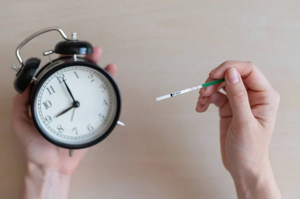 Kvinnan håller ett positivt graviditetstest och väckarklocka. Nio månaders graviditet. Begreppet biologisk klocka fertilitet. Två ränder. — Stockfoto