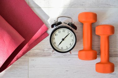 Turuncu halterli çalar saatin ve ahududu yoga minderinin üst görüntüsü. Karantina sırasındaki ev sporları konsepti. Fitness zamanı. Dersler için erken kalkış.
