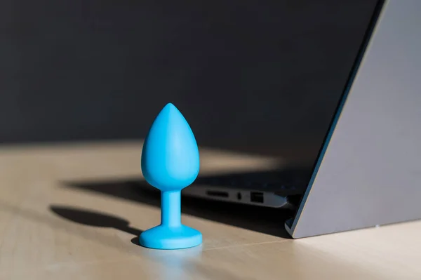 Blue latex anal plug the laptop on the table. The concept of virtual sex on the Internet. Anus extender toy for adults.