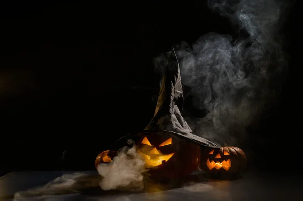 Strašidelné oranžové dýně na Halloween stojí v řadě na tmavém pozadí. Jack O Lantern v čarodějnickém klobouku. Záhadná mlha se plazí po zemi. Trick or treat. — Stock fotografie