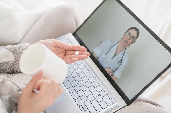 Невпізнавана жінка п'є таблетки, як це передбачено лікарем на онлайн-консультації. Жінка-лікар розмовляє з хворим пацієнтом на веб-камеру. Дівчина з грипом на хворій відпустці . — стокове фото