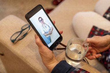 Online tıp karantinada. Koronavirüs semptomları olan yaşlı bir kadın bir virüs uzmanıyla görüntülü konuşma yapıyor. Bir emekli sıcaklığı ölçer. Doktora telefonla uzaktan danışma.