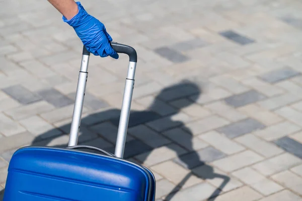 Close-up van een vrouwelijke hand in een handschoen op een handvat. Er loopt een vrouw op straat met een grote blauwe tas. Reisconcept tijdens een virusuitbraak. Persoonlijke hygiëne — Stockfoto