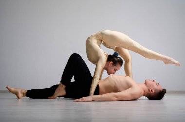 Çift numarası gösteren bir akrobat düeti. Jimnastik yapan bir kadın, gömleksiz bir adamın üstünde amuda kalkarak tulum giyer. Çok esnek sirk sanatçıları..