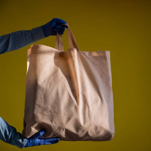 Sending eco-friendly reusable cotton bag on a yellow background. The courier holds a canvas fabric bag without plastic packaging on a yellow background. Safe delivery to the epidemic. — Stock Photo, Image