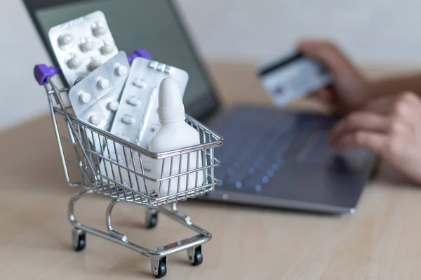 Online pharmacy concept. A woman holds a credit card in her hands and buys pills online. A girl makes an online purchase of medicines with home delivery on a laptop.