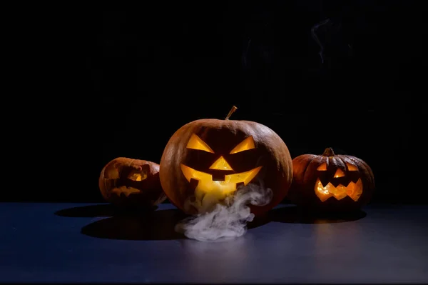 Halloweenská karta. Jack o lucerna se svíčkami zářit na černém pozadí. Řada strašidelných dýní s vyřezávanými grimasami kouří ve tmě. — Stock fotografie