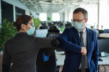 Ofiste buluşurken iki meslektaş el sıkışmaktan kaçınır ve dirsek tokuşturur. Wuhan 'da selamlar. Tıbbi maskeli bir adam ve bir kadın iş yerinde sosyal bir mesafeyi koruyorlar..