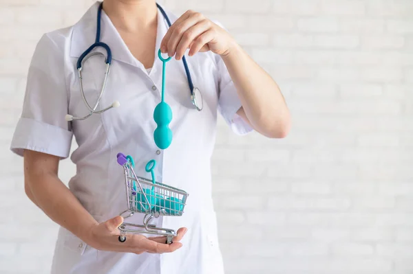 A faceless gynecologist puts a set of vaginal balls into a miniature shopping cart. The doctor holds a mini trolley and device for the muscles of the pelvic floor. Female health concept. Kegel toy